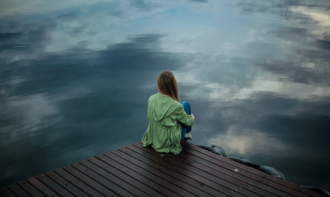 Osamělá dívka sedí na molu
