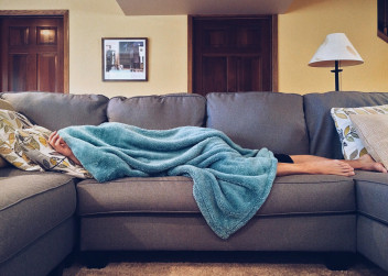 Unavená žena leží na gauči přikrytá dekou